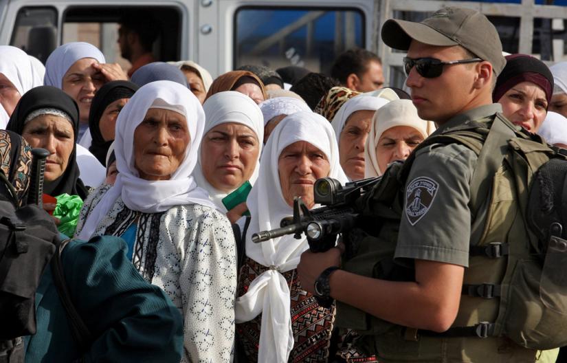 An Israeli soldier stands guard over Palestinians waiting to cross at a checkpoint